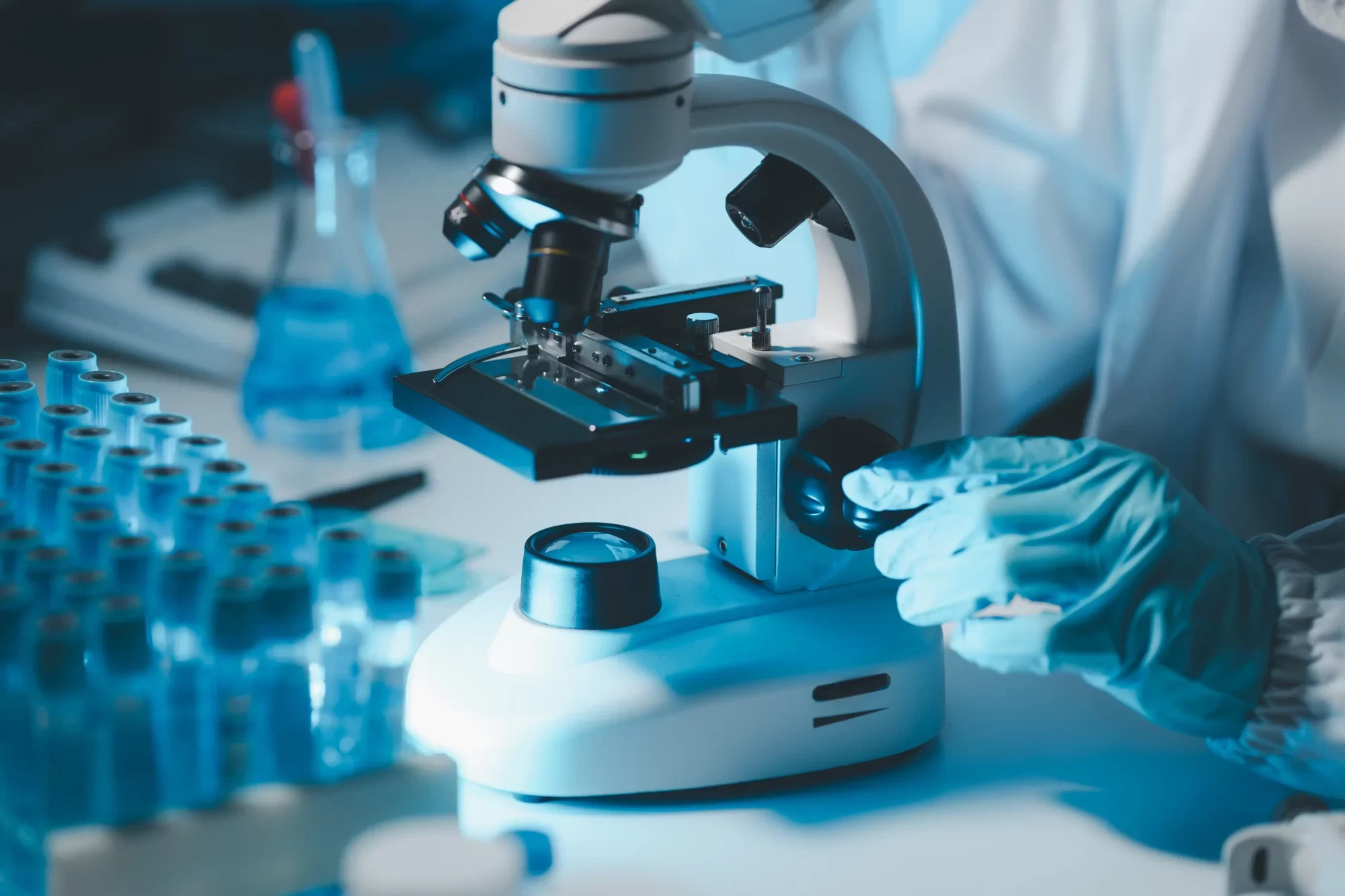 A scientist in gloves uses a microscope in a laboratory.