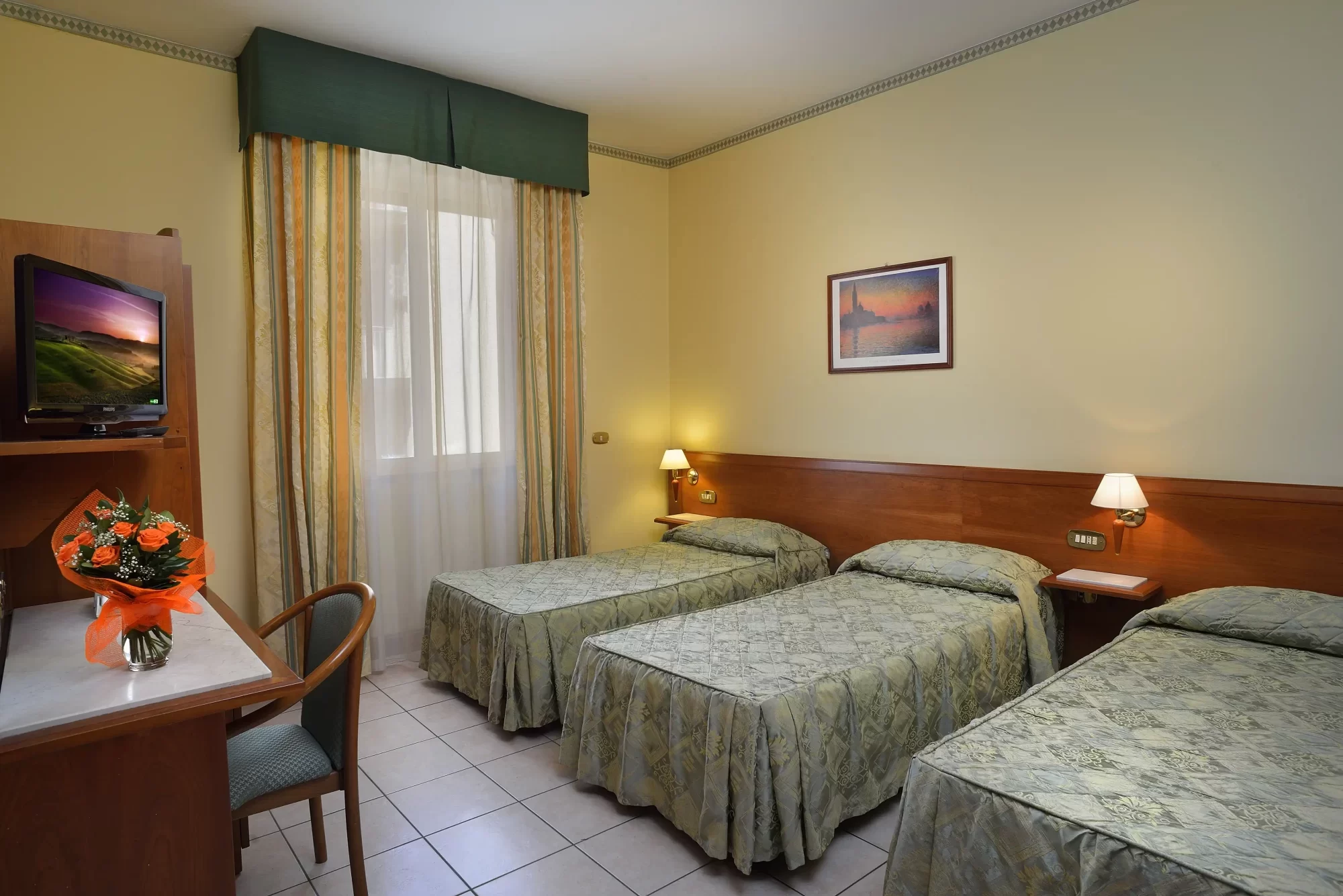 Camera d'albergo con tre letti singoli, scrivania e decorazioni semplici.