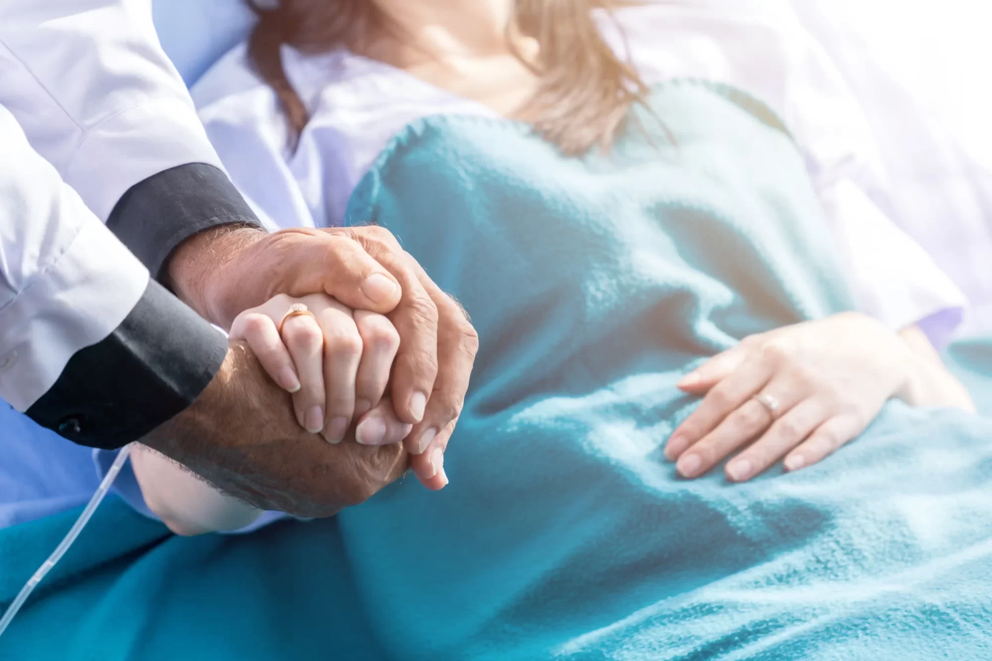 Medico che tiene la mano di un paziente ricoverato a letto.