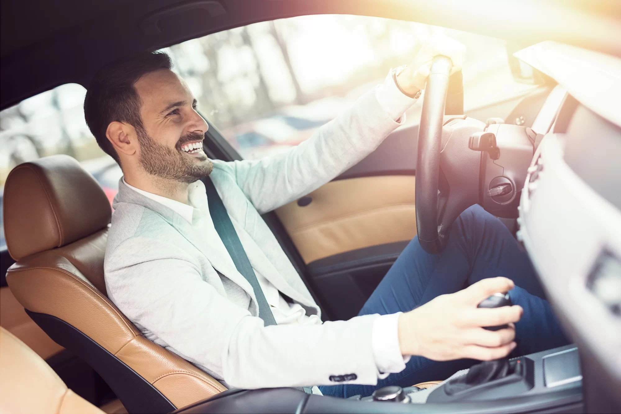 Uomo sorridente che guida un'auto con interni eleganti.