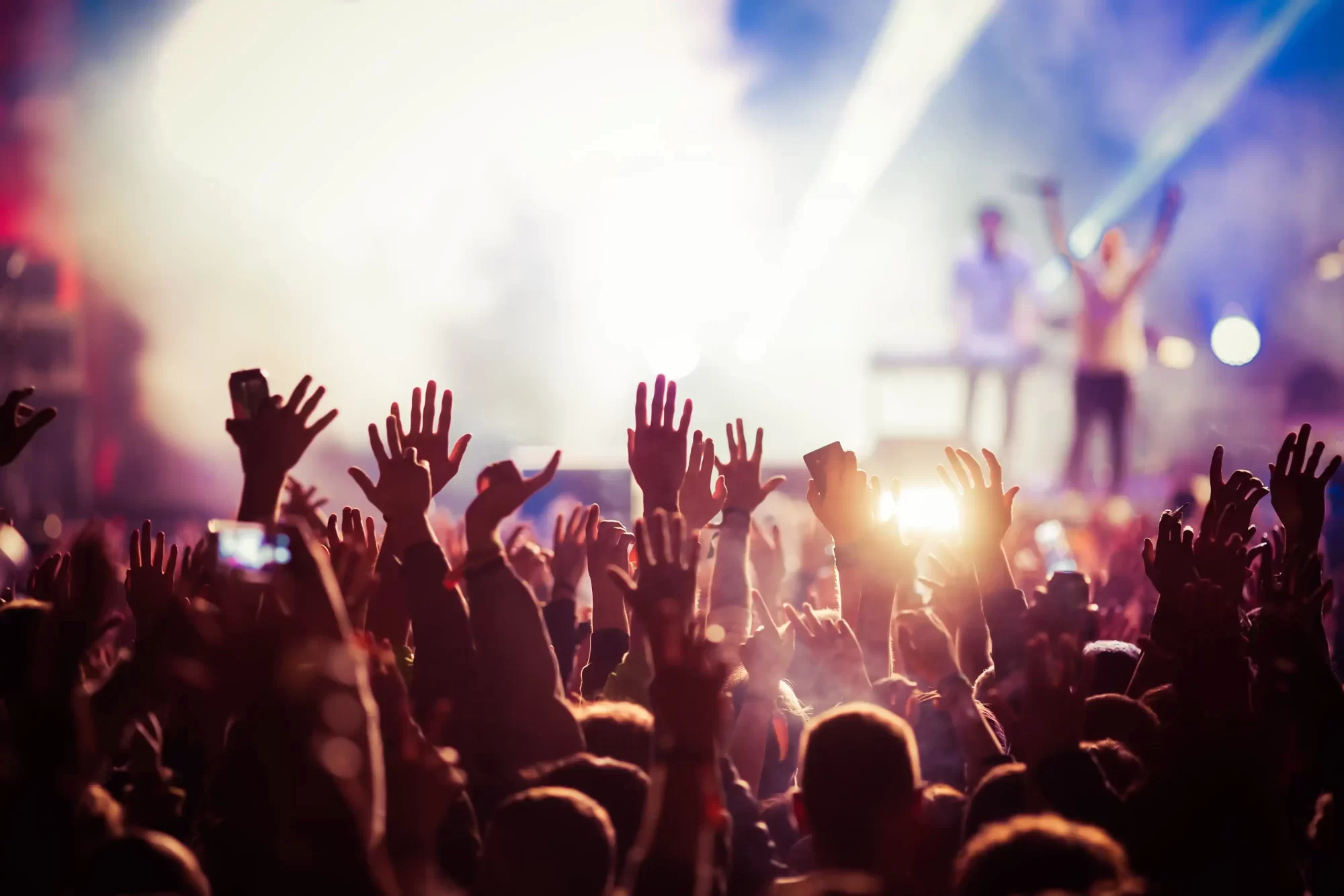 Folla di persone che alzano le mani durante un concerto con luci colorate sul palco.